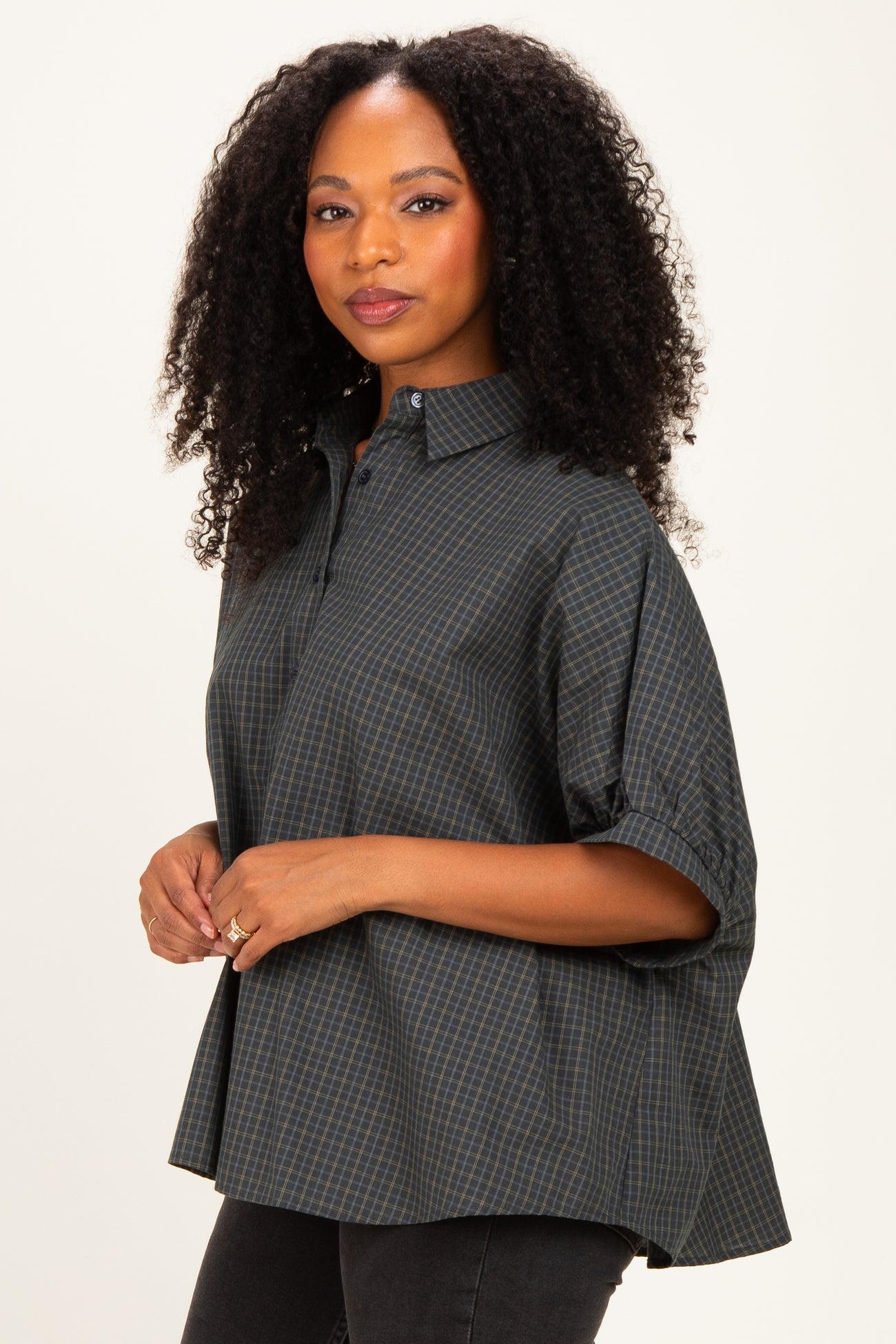 woman wearing a dark green checkered oversized button-up shirt with rolled sleeves and a relaxed fit