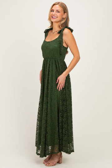 woman wearing a dark green lace maxi dress with tie straps and a fitted waist, smiling at the camera