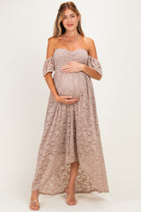 woman wearing a beige off-the-shoulder lace maternity dress and holding her baby bump