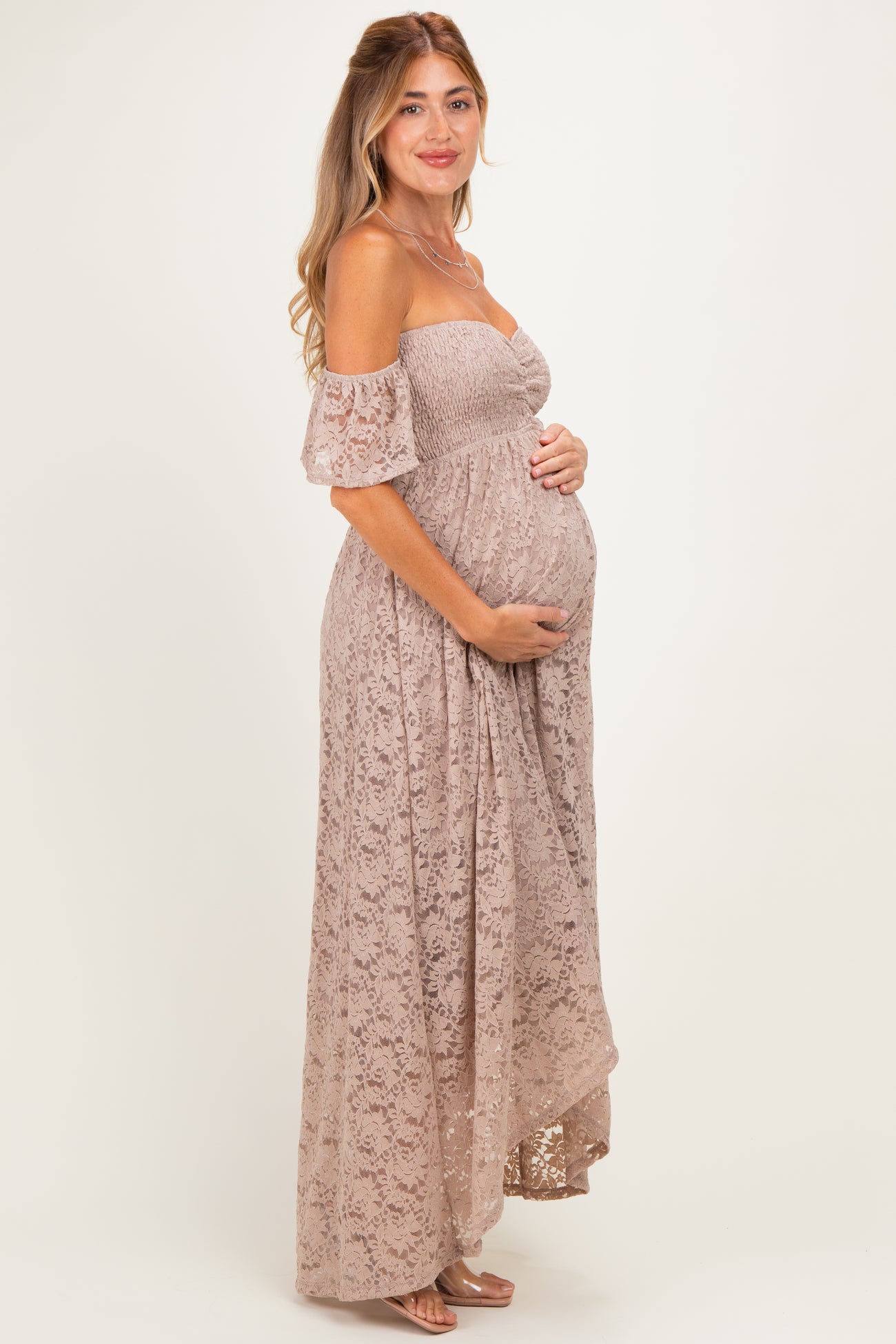 woman wearing a dusty rose off-shoulder maternity gown with lace details and holding her baby bump