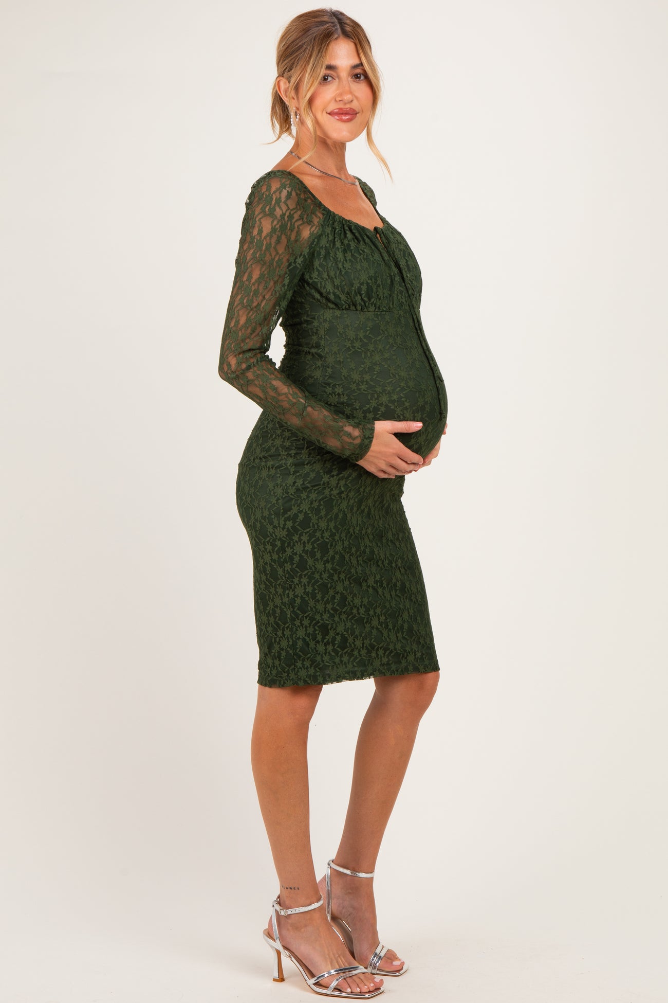woman wearing a dark green lace maternity dress, fitted style, showing her baby bump with long sleeves and a sweetheart neckline