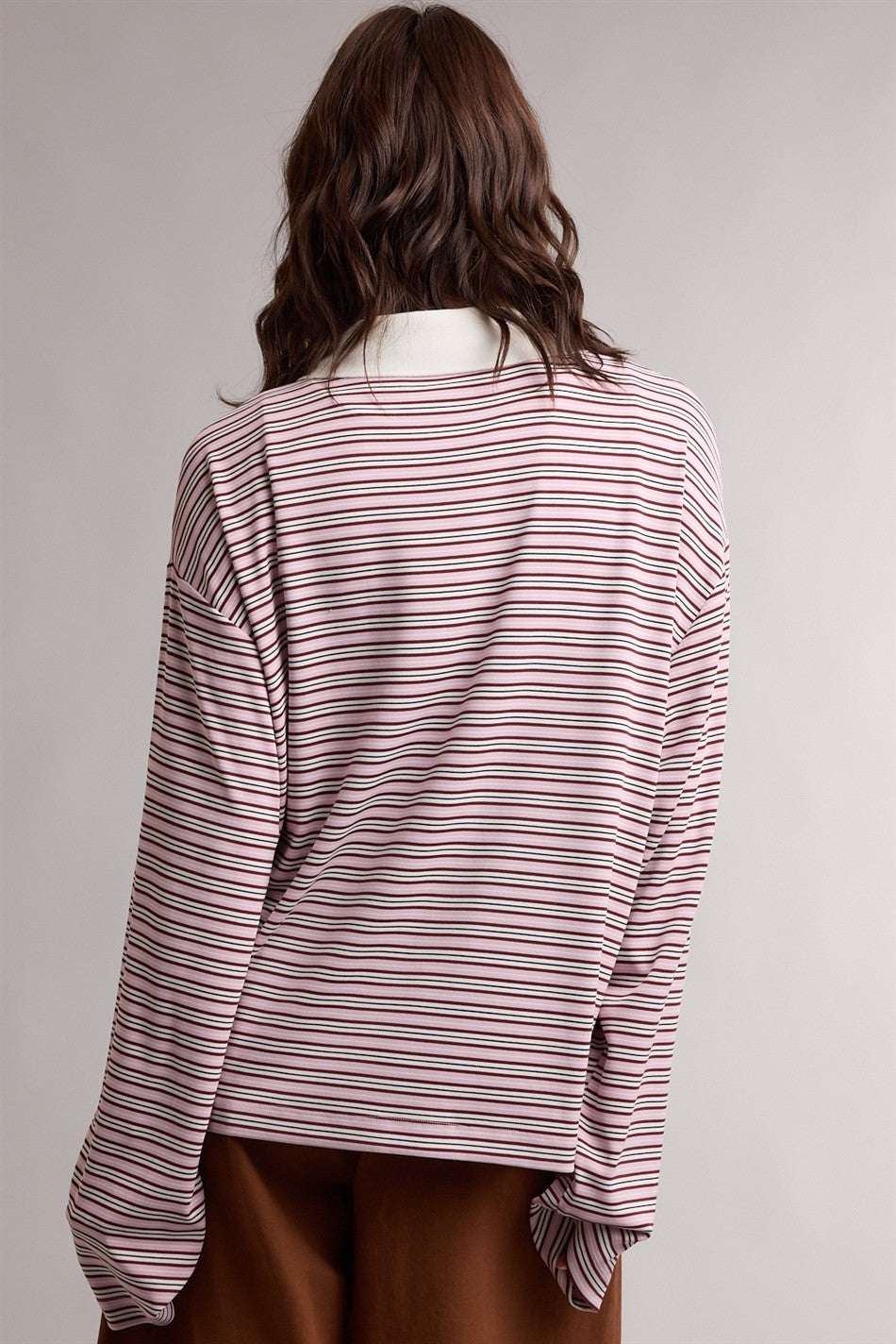 woman wearing a pink and white striped long sleeve top with a relaxed fit and wide sleeves, viewed from the back