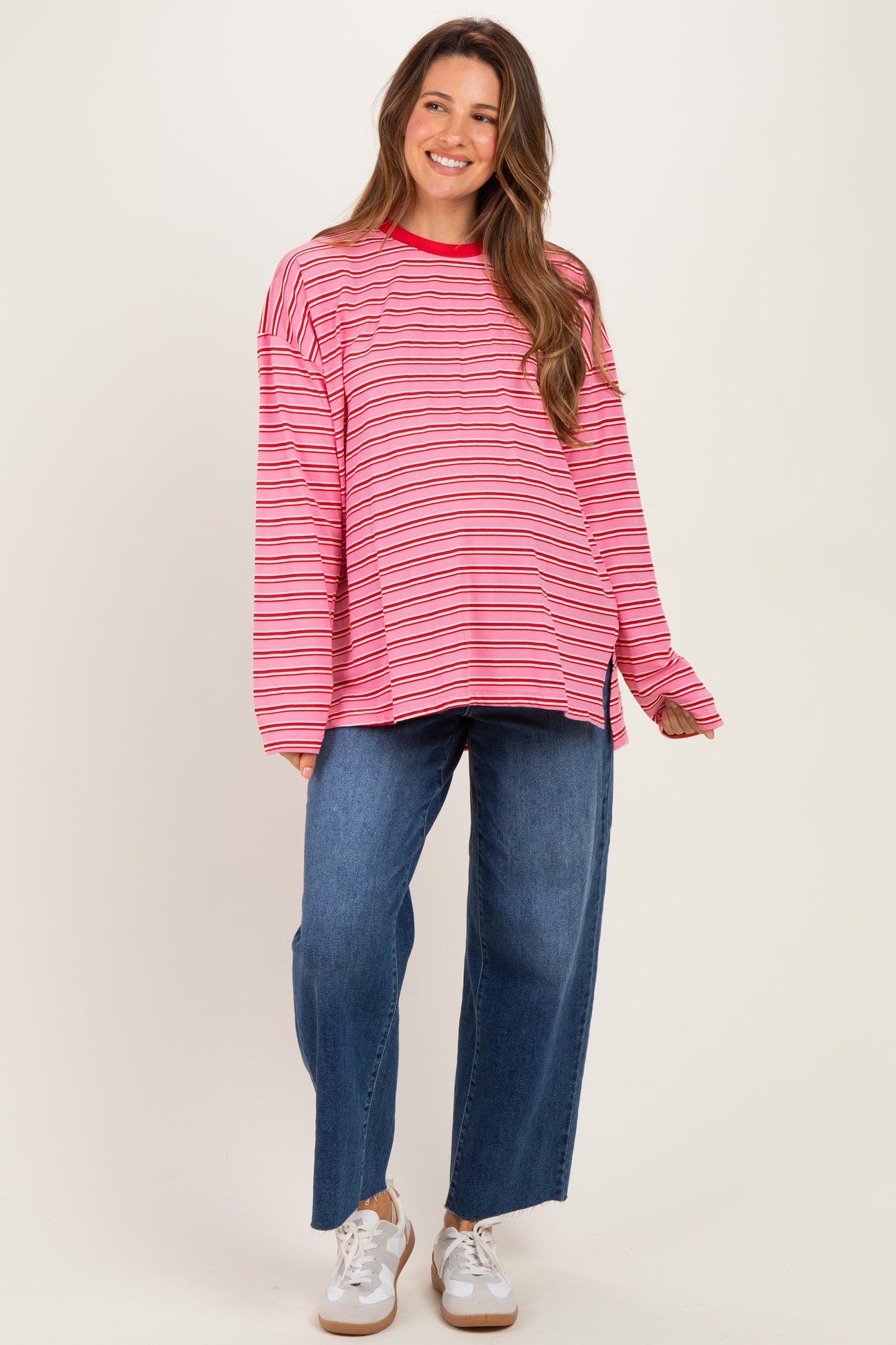 woman wearing a pink and red striped maternity top with long sleeves paired with wide-leg blue jeans