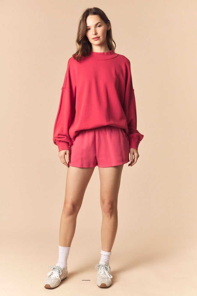woman wearing a pink oversized sweatshirt and matching shorts with white sneakers and ankle socks