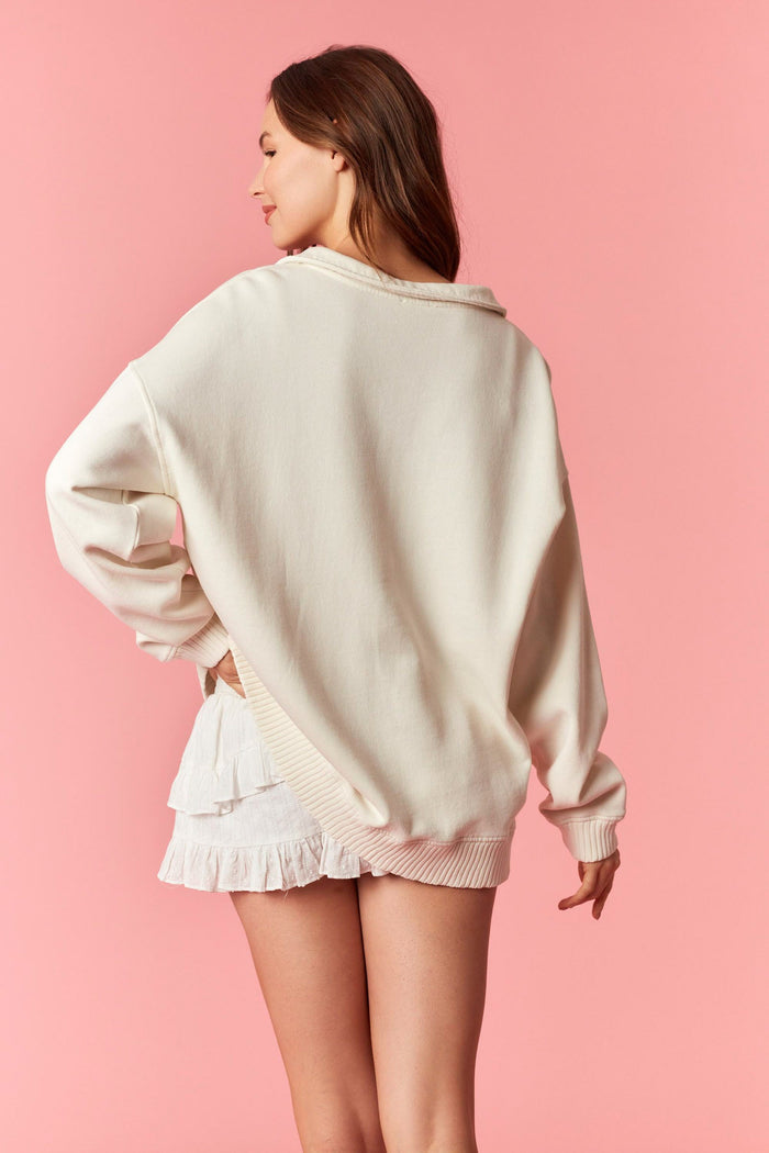 woman wearing a relaxed fit cream sweatshirt with a loose collar and side slits paired with white ruffled shorts