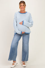 woman wearing a blue and white striped maternity sweater and holding her baby bump, paired with wide-legged jeans