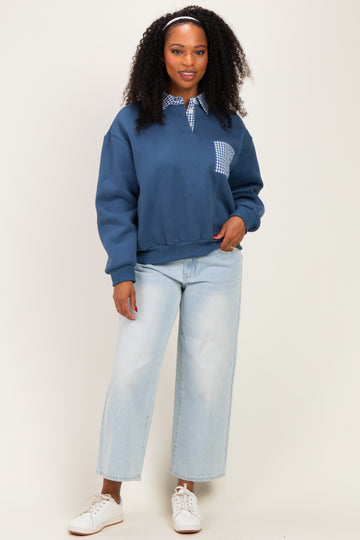 woman wearing a navy blue sweatshirt with a checkered pocket and light wash wide-leg jeans, smiling