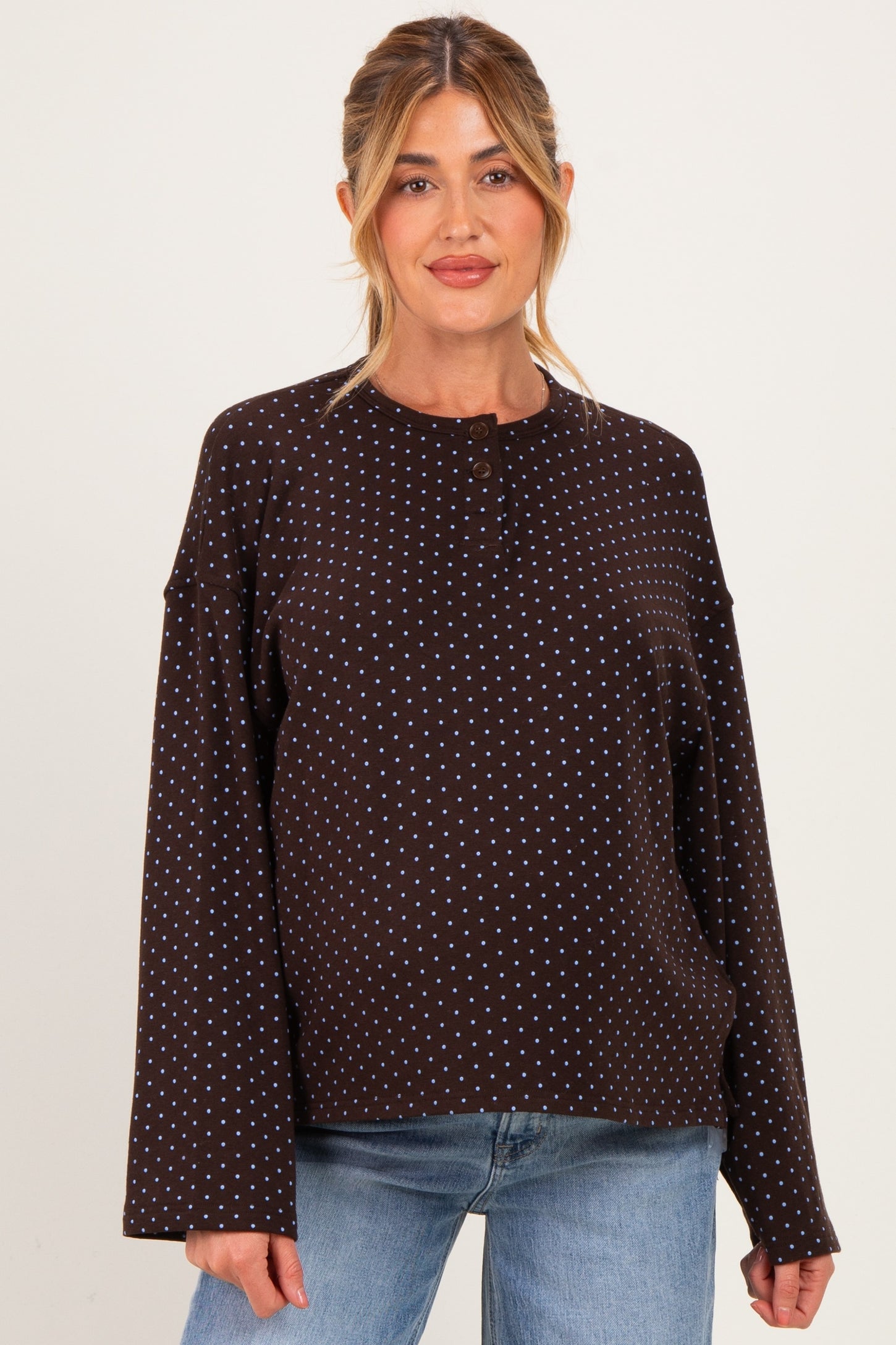 woman wearing a brown polka dot maternity top with button details and long sleeves, styled with light blue jeans