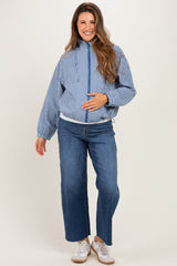 woman wearing a blue and white gingham maternity jacket and blue wide-leg jeans, gently cradling her baby bump