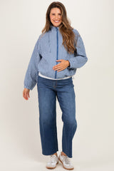 woman wearing a blue and white gingham maternity jacket and blue wide-leg jeans, gently cradling her baby bump