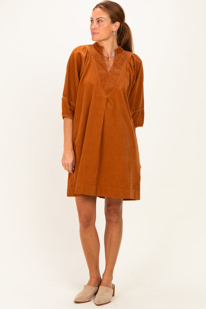 woman wearing an orange corduroy tunic dress with a v-neck and three-quarter sleeves, standing in a relaxed pose