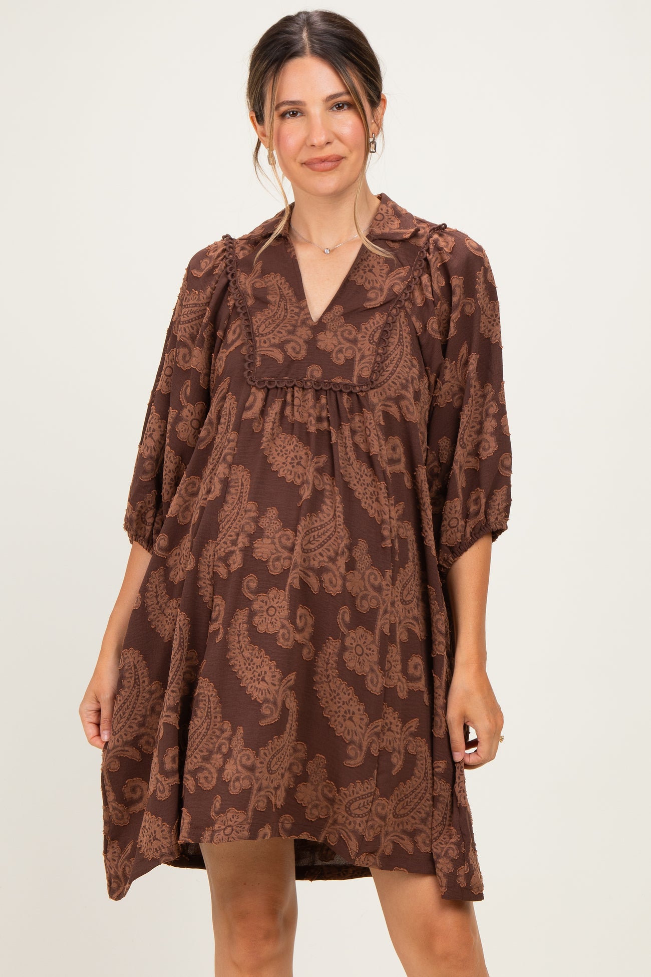 woman wearing a brown paisley print maternity dress with a v-neck and 3/4 sleeves, gently draping over her baby bump