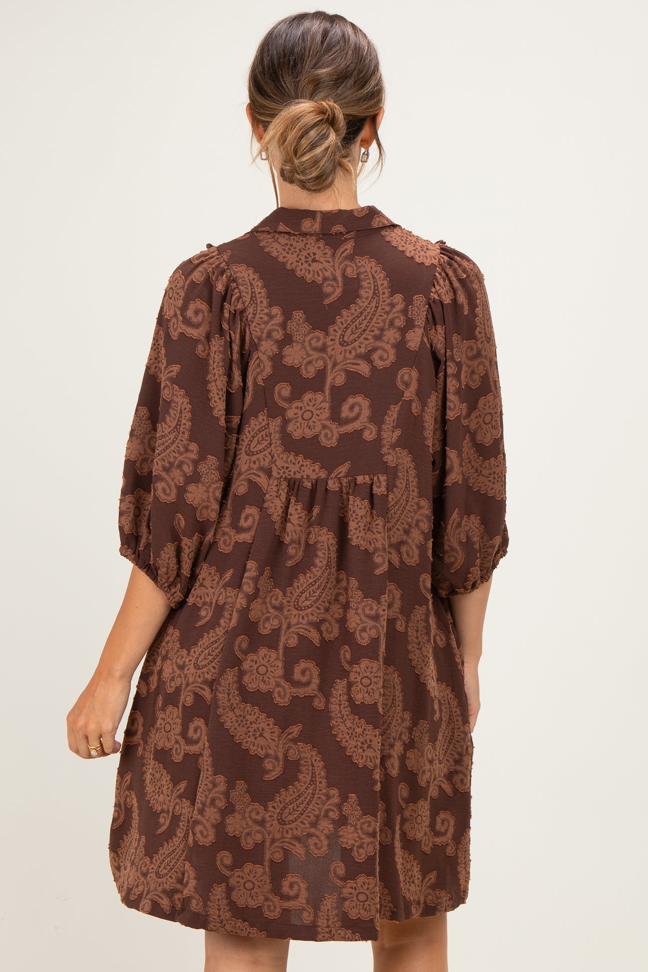 woman wearing a brown paisley print maternity dress with a loose fit and puff sleeves from the back