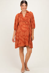 woman wearing a rust-colored maternity dress with a paisley print and puff sleeves, showing her baby bump