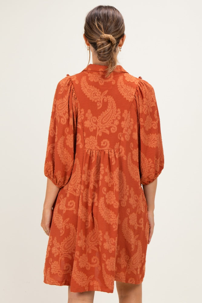 woman wearing a rust-colored maternity dress with puff sleeves and paisley print, showing back view