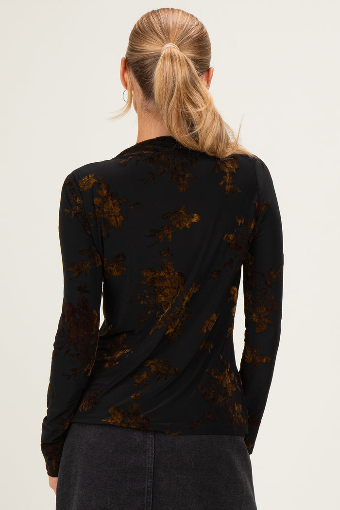 woman wearing a black long sleeve top with a floral print in shades of brown and gold, seen from the back