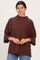 woman wearing a brown oversized sweater with a high neckline and wide sleeves, standing against a light background