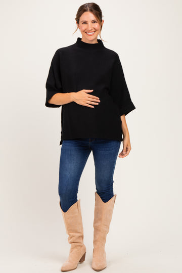 woman wearing a black short sleeve maternity top and holding her baby bump with blue jeans and beige boots
