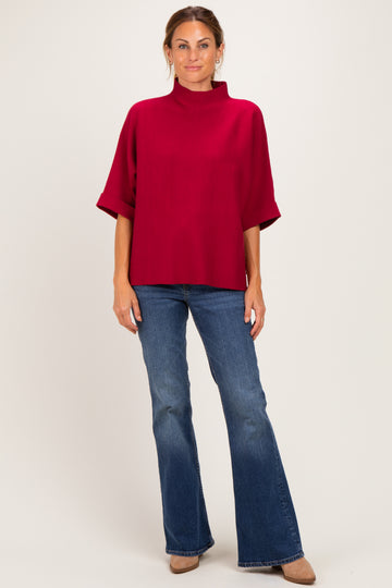 woman wearing a burgundy mock neck top with wide sleeves and blue flared jeans