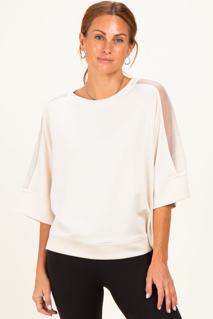 woman wearing a cream oversized sweatshirt with sheer details on sleeves and relaxed fit with black leggings