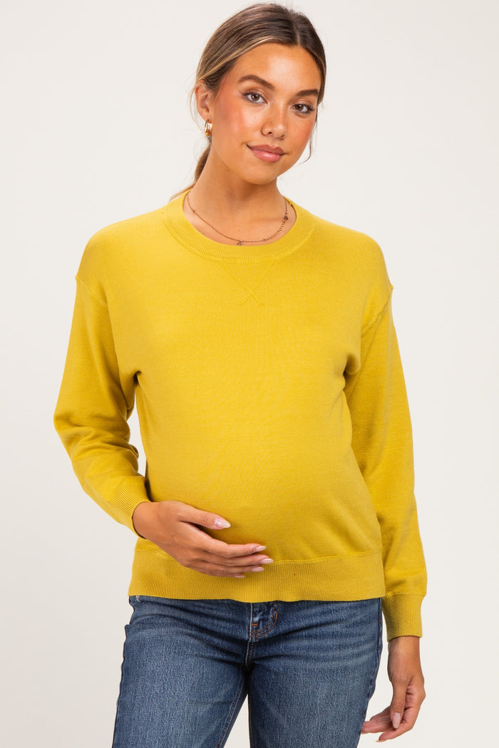 woman wearing a mustard yellow long sleeve maternity sweater and holding her baby bump