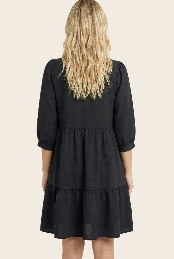 woman wearing a black tiered dress with three-quarter puff sleeves, shown from the back