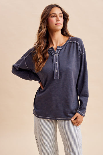 woman wearing a navy blue long sleeve henley top with buttons and relaxed fit, paired with striped pants