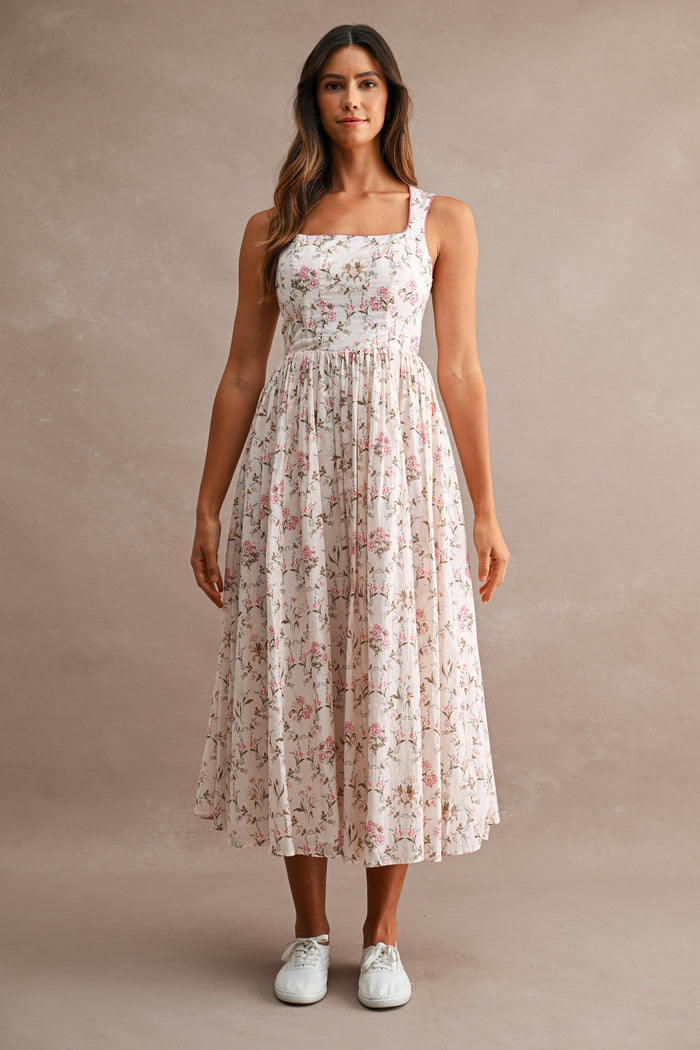woman wearing a floral print midi dress with a square neckline and a flowy skirt, paired with white sneakers