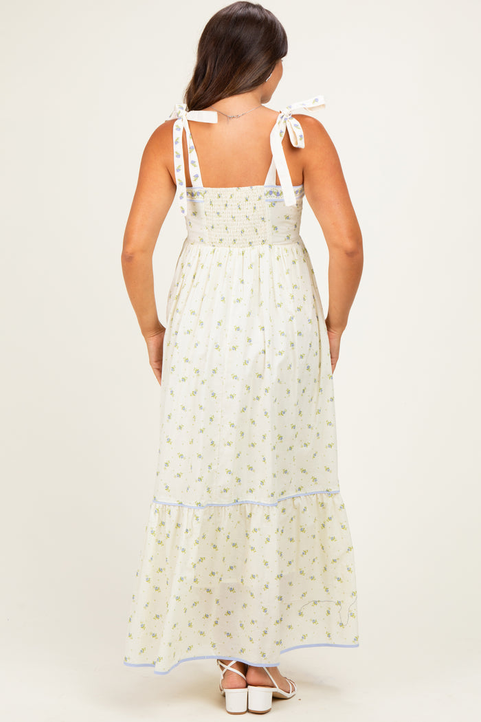woman wearing a white floral print maternity maxi dress with tie straps, showcasing a smocked bodice and tiered skirt