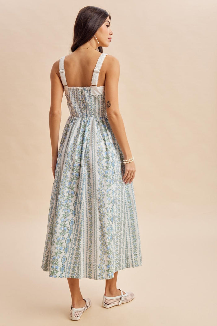 woman wearing a blue and white floral maxi dress with a smocked back and wide straps, seen from the back