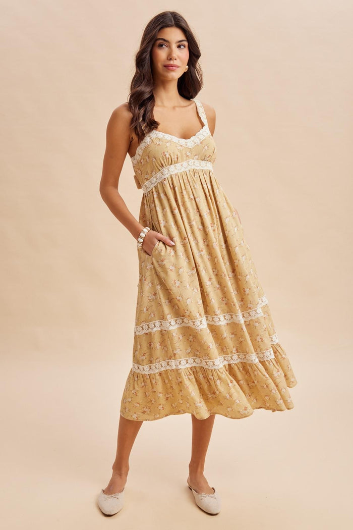 woman wearing a yellow summer dress with floral print and lace trim, featuring pockets and a flared hem