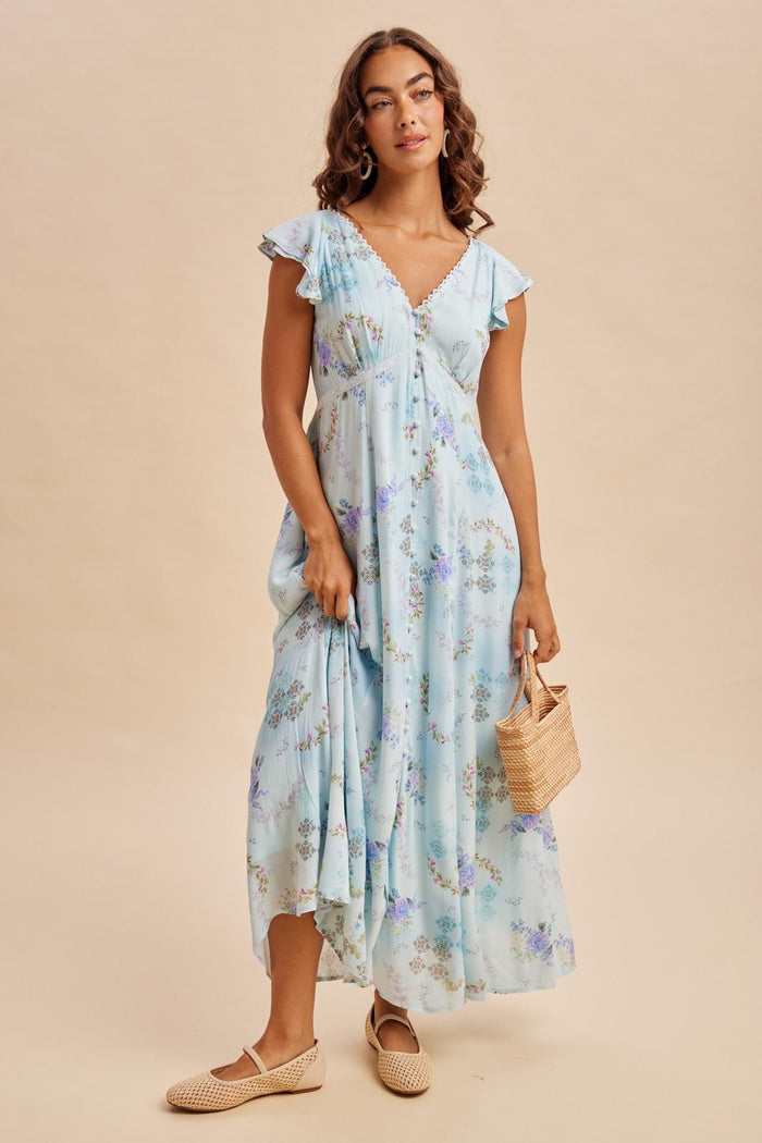 woman wearing a light blue floral maxi dress with flutter sleeves and holding a straw bag