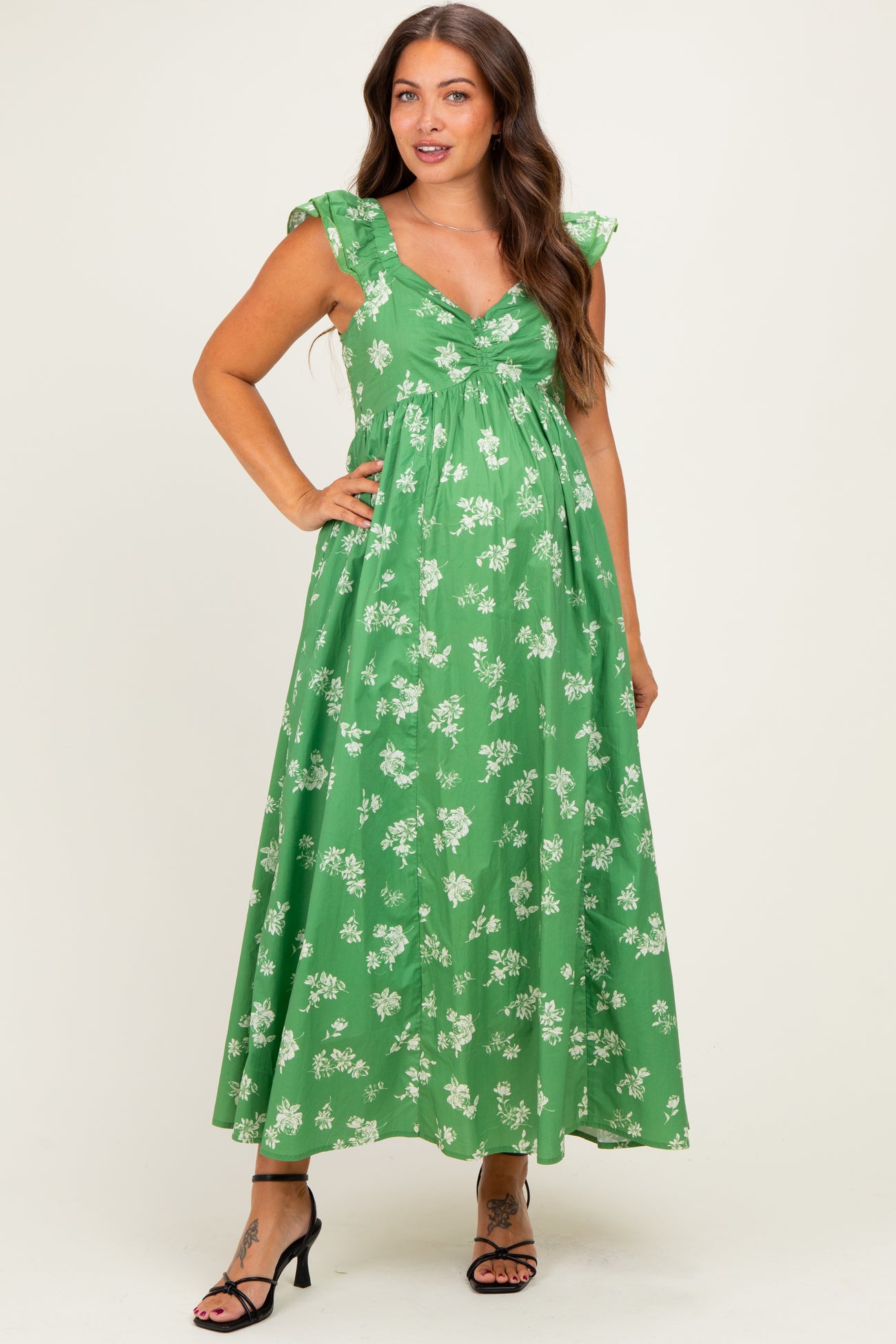 woman wearing a green floral maternity maxi dress with cap sleeves and a twist front detail, smiling and posing.