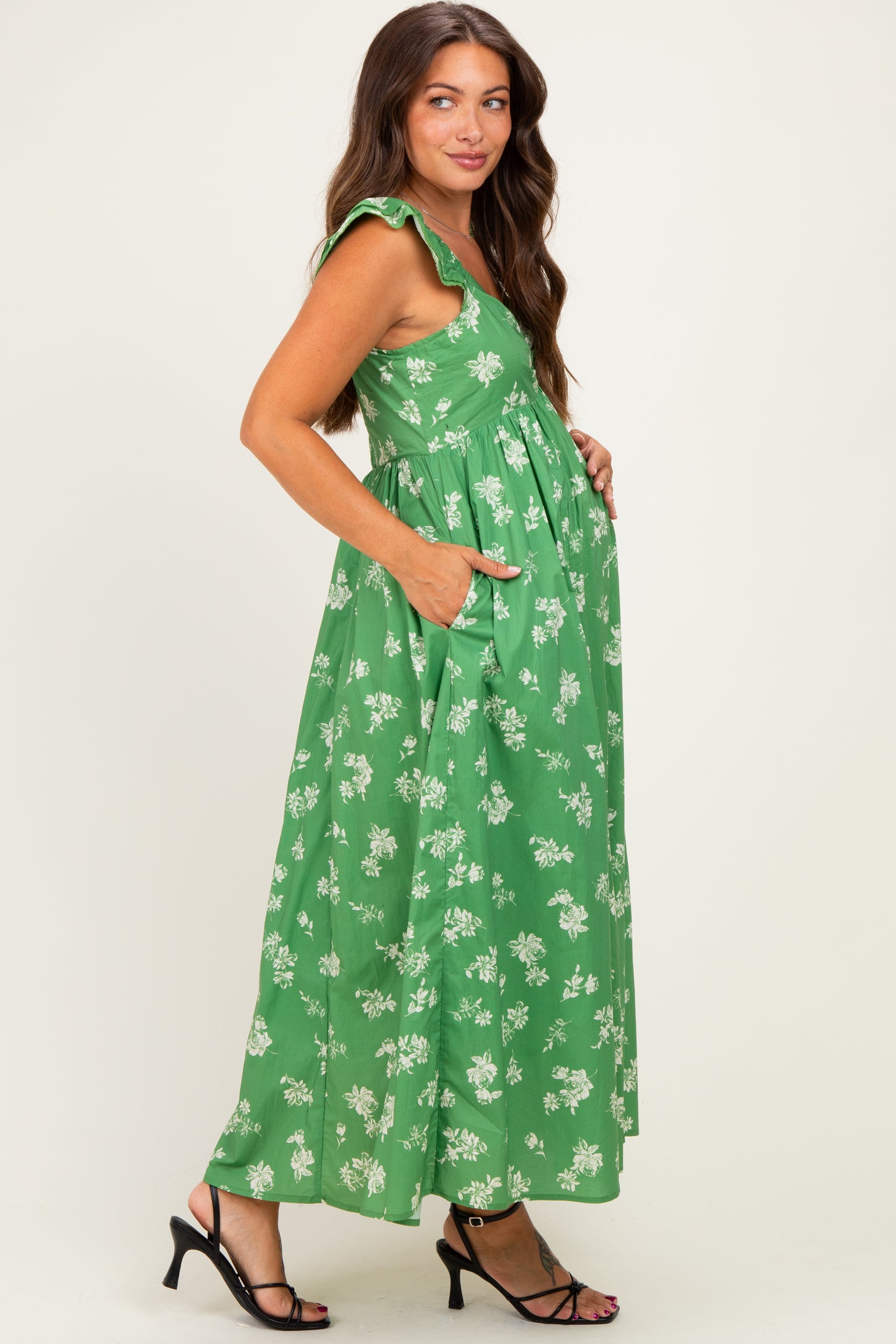 woman wearing a green floral maternity maxi dress with ruffled sleeves and pockets, showcasing her baby bump