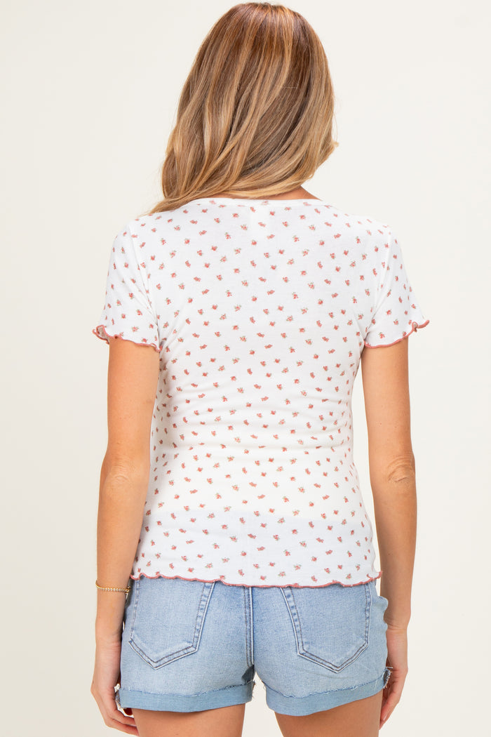 woman wearing a white maternity top with a floral pattern and ruffled short sleeves, paired with denim shorts
