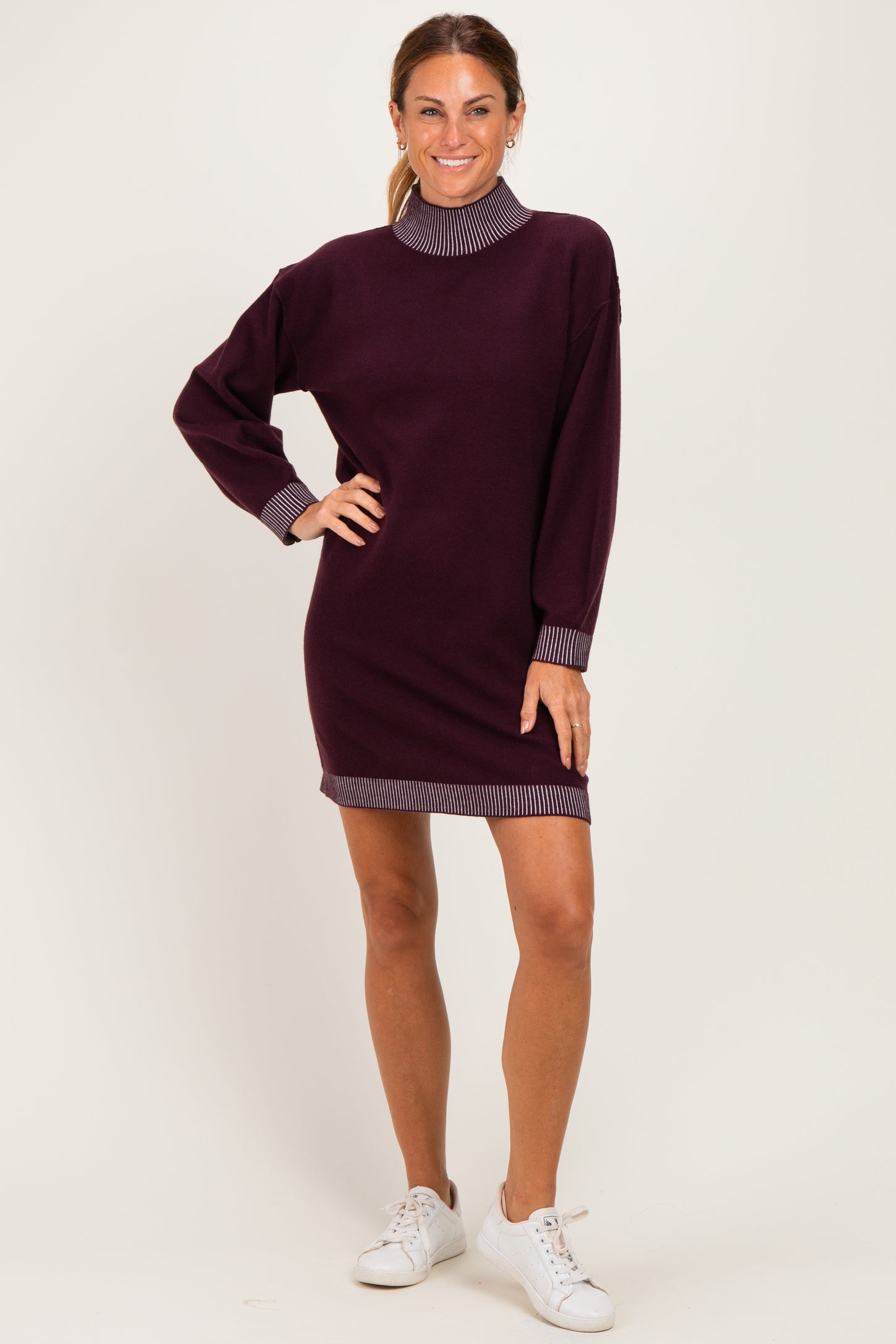 woman wearing a burgundy long sleeve sweater dress with striped collar and cuffs, paired with white sneakers