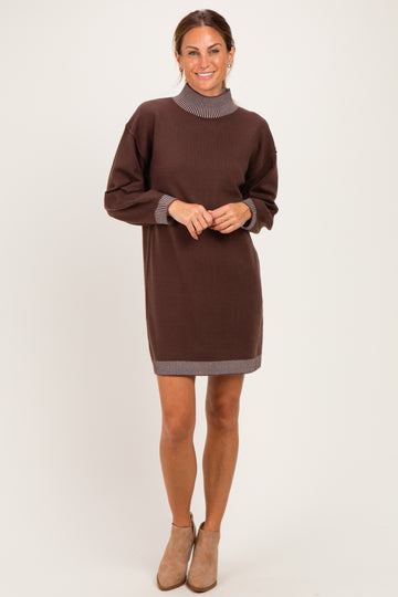 woman wearing a brown sweater dress with a ribbed collar and cuff details, standing and smiling