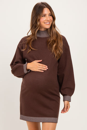 woman wearing a brown maternity sweater dress with striped details and holding her baby bump