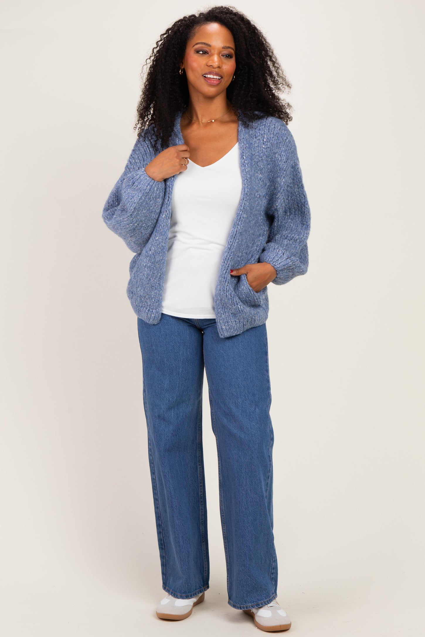 woman wearing a light blue oversized knit cardigan over a white top and blue wide-leg jeans