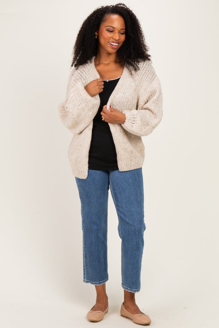 woman wearing a cream chunky knit cardigan over a black tank top and blue straight-leg jeans with beige flats