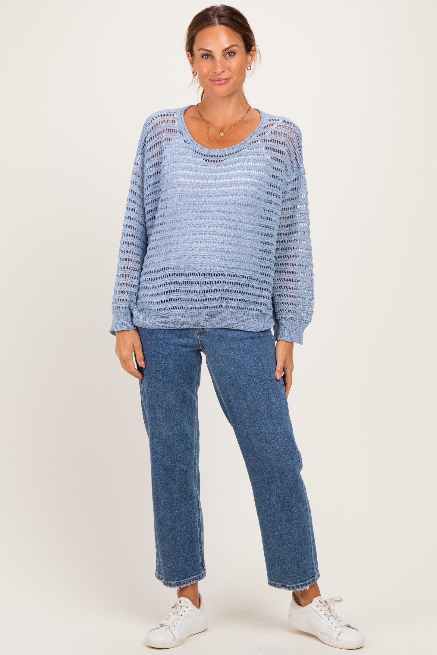 woman wearing a light blue open knit sweater and blue jeans with white sneakers