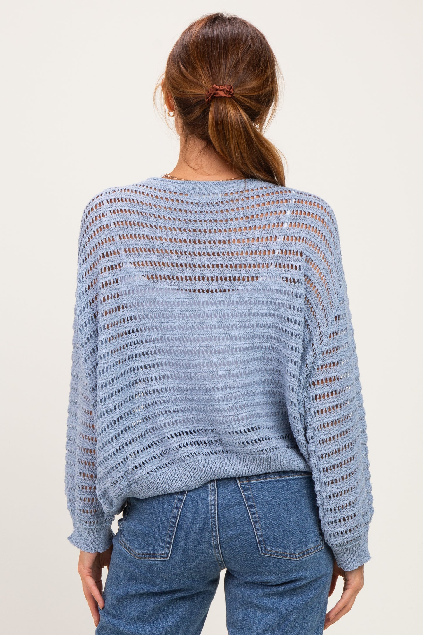 woman wearing a light blue open-knit sweater with a relaxed fit and long sleeves, styled with high-waisted jeans