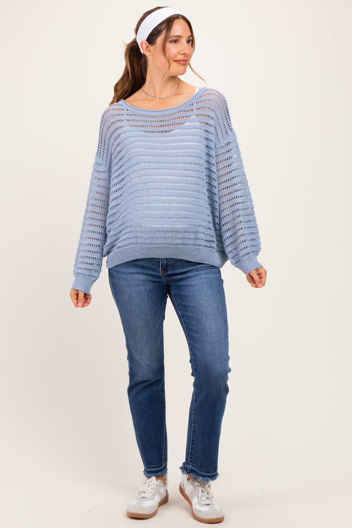 woman wearing a light blue maternity sweater with open knit patterns, paired with blue jeans and white sneakers