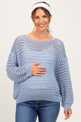 woman wearing a light blue maternity sweater with open knit design, smiling and holding her baby bump