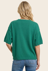 woman wearing a green short sleeve sweater with a relaxed fit and ribbed hem, styled with light blue jeans
