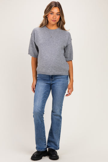 woman wearing a grey maternity sweater and blue flared jeans, with no visible baby bump