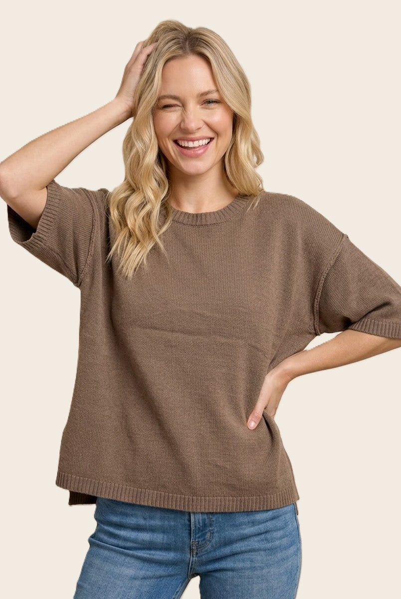 woman wearing a brown short sleeve oversized sweater and smiling while posing with one hand on her head