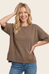 woman wearing a brown short sleeve oversized sweater and smiling while posing with one hand on her head