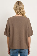 woman wearing a loose-fitting brown knit sweater with short sleeves, viewed from the back, paired with blue jeans