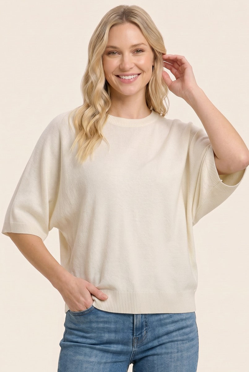 woman wearing a soft cream oversized sweater with batwing sleeves and a relaxed fit, paired with light blue jeans